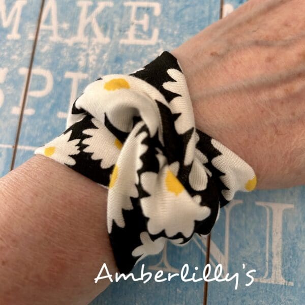 Daisy look print fabric bracelet with background of fabric black and flowers are white petal with yellow middle set against a blue background