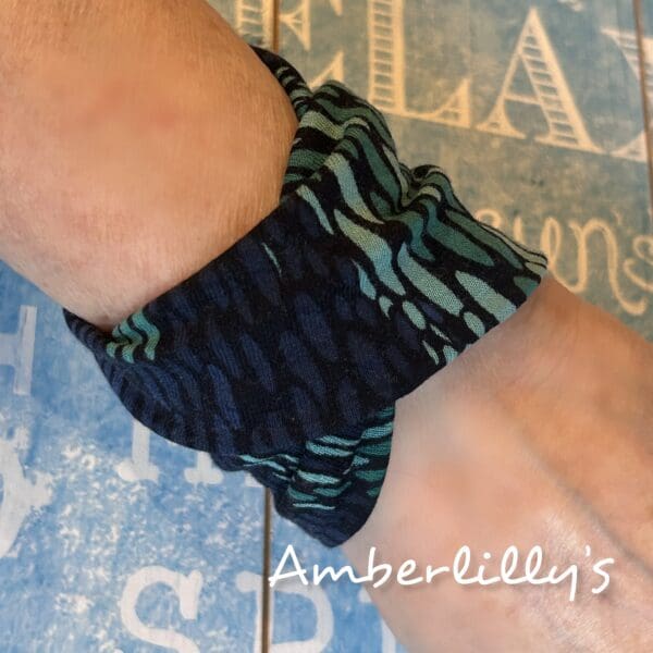 Green striped cuff bracelet worn by creator with a blue backdrop