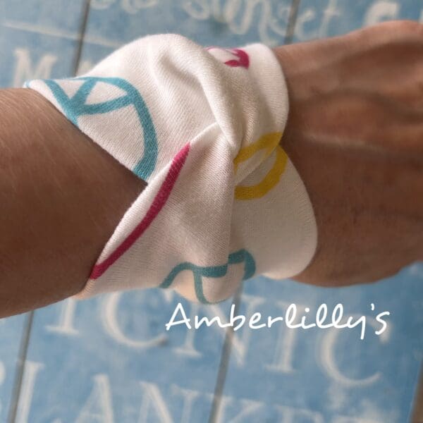 Wrist fabric cuff bracelet with peace sign design in different colours with a white background creates. Modelled by creator against a blue backdrop