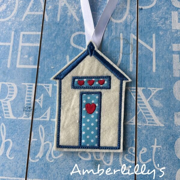 Beach hut made with felt and machine embroidered. Main colour is cream with turquoise polka dot fabric door and over door panel with red hearts. Approx 6x10 cm not included white ribbon to hang it.