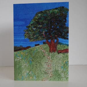 Front view of greetings card showing oak tree in summer foliage near top of grassy hillside.