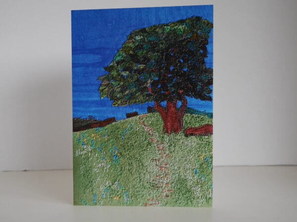 Front view of greetings card showing oak tree in summer foliage near top of grassy hillside.