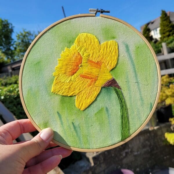 Bright yellow single daffodil hand embroidered on watercolour background 6 inch hoop wall hanging.