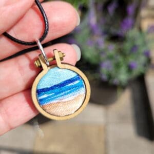 Hand embroidered seascape set in a mini embroidery hoop measuring 2.5cm with a choice of leather or silver necklace.