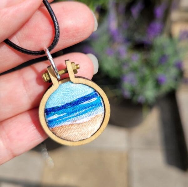 Hand embroidered seascape set in a mini embroidery hoop measuring 2.5cm with a choice of leather or silver necklace.