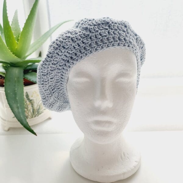 Handmade pastel blue crochet beret hat made by Sarah Lou Crafts, displayed on a neutral background.