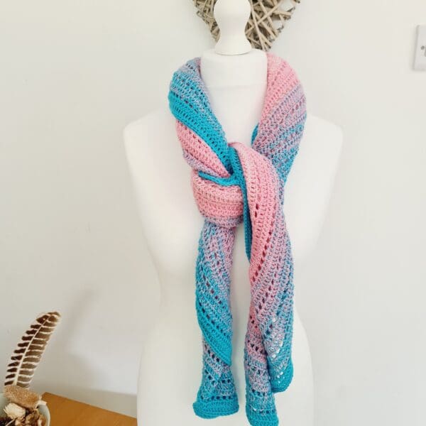 Detail of the fringed edge of a crochet triangle scarf, featuring the beautiful light blue, pink, and white stripes of the Transgender Pride flag. Shown as a tied scarf, made by Sarah Lou Crafts.
