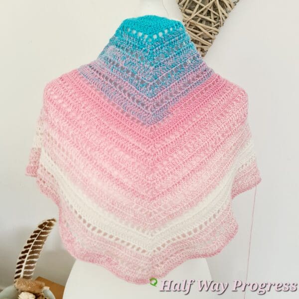 A soft, textured crochet shawl, hand-crafted by Sarah Lou Crafts in the distinctive light blue, pink, and white colours of the Transgender Pride flag.