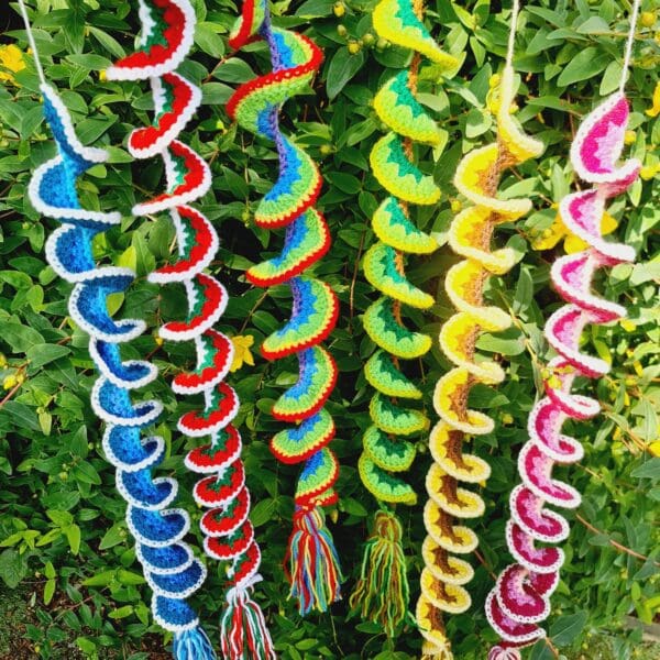 Wind Spinners made by Sarah Lou Crafts in six different designs of and colours shown hanging from a green garden bush as ornaments and can also be used as window hangings.