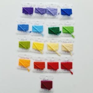 Yarn colour samples on bobbins that will be used to make a crochet temperature blanket by Sarah Lou Crafts. Top row starts with purples moving through the spectrum to red at the bottom. 