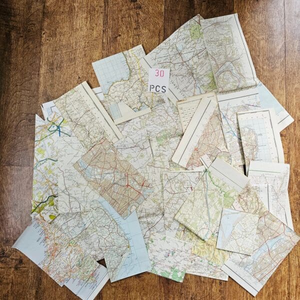 A wide shot of various sized and irregularly shaped pieces of vintage maps, some with city names and roads visible, fanned out on a wooden background.