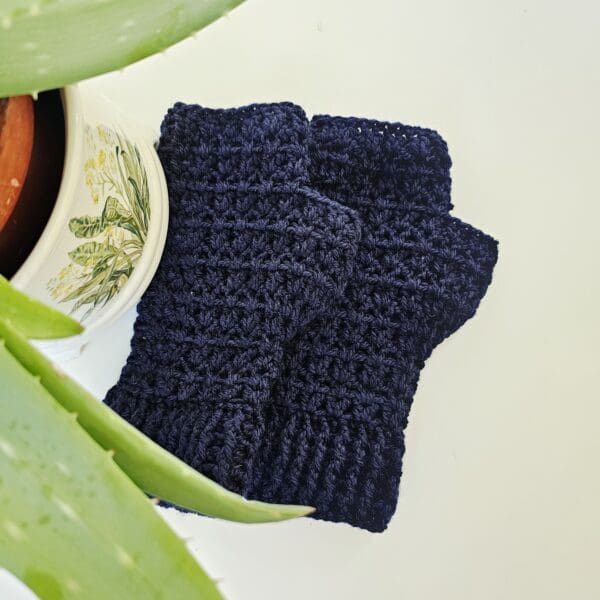 A close-up of the textured stitch pattern of a navy blue crochet fingerless mitt, with a blurred hiking map in the background. This image highlights the intricate crochet work and the quality of the yarn, while the background provides context.