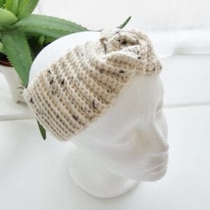 An angled view of the cream and black speckled crochet ear warmer headband on a white mannequin head. This angle shows the continuous pattern and how the headband seamlessly wraps around the back of the head.