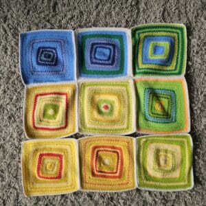 Flat lay of crochet squares with different coloured rows in blues, reds, yellow and greens to show the top temperature taken at 12 pm each day in Carmarthenshire, Wales for the months of January to September 2025.