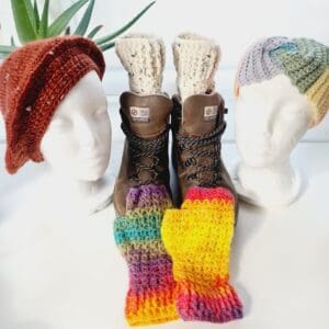 A collection of hand-crocheted adventure accessories winter gear for outdoor enthusiasts, including berets, boot cuffs, ear warmers, and fingerless gloves in various colours and textures.
