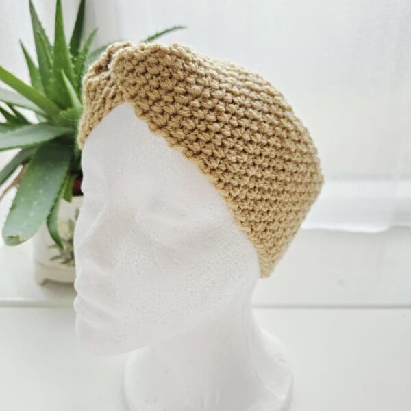 Full view of a thick, cosy, sand-coloured aran yarn ear warmer being worn on a display head.