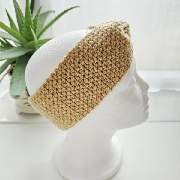 Detailed shot of the crochet stitching showing the moss pattern of a sand-hued ear warmer headband.