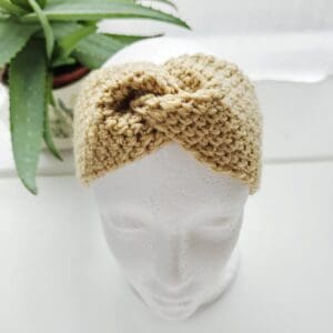 Crocheted ear warmer headband in sand coloured aran yarn, shown on a white mannequin head.