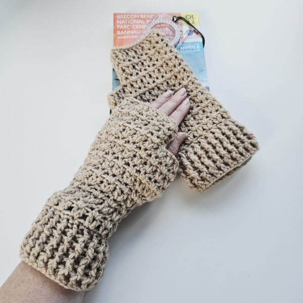 The texture of the light brown yarn is clearly visible in these crochet fingerless mitts, placed on a white table next to a folded OS map.