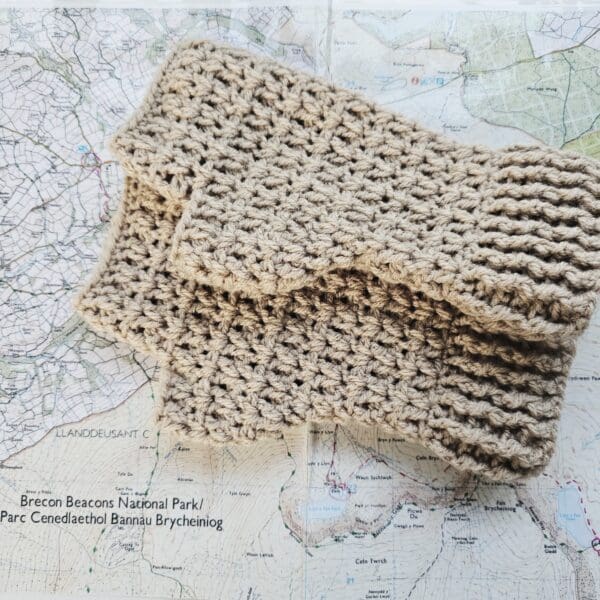 Close-up of a pair of light brown crochet fingerless mitts lying next to a vintage map and a compass.