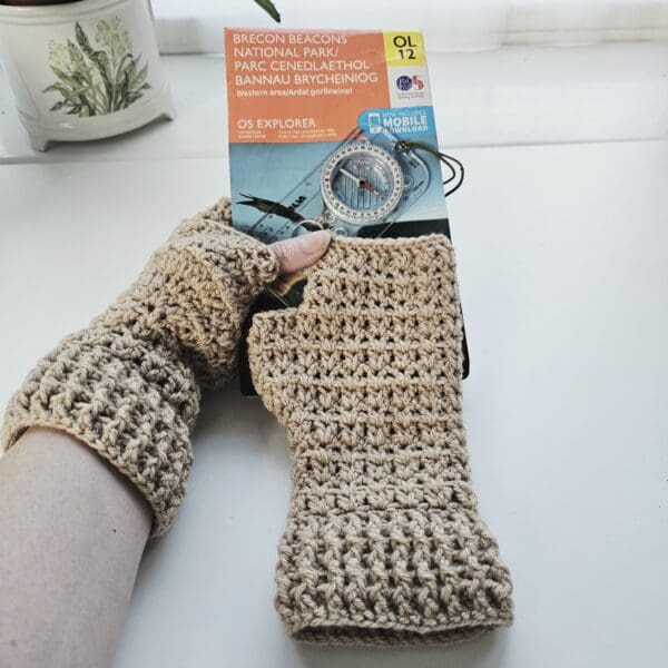 One fingerless mitt in a light brown, coffee colour resting on an OS map with a hiking compass in the background.