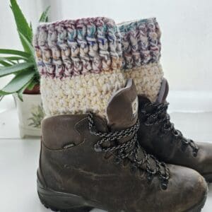 Close-up of a pair of handmade crochet boot cuffs in a vibrant multicoloured yarn, extending above the top of brown hiking boots.