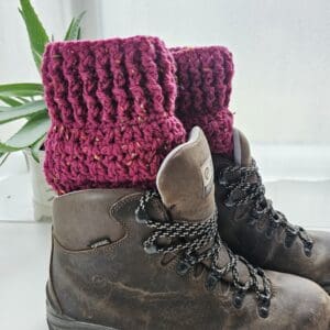 Crochet boot cuffs in a rich berry red aran yarn, worn over the top of brown leather hiking boots.