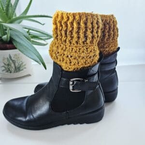 Close-up of a crocheted boot cuff in bright yellow aran yarn, featuring a textured stitch pattern, worn with black ankle boots.