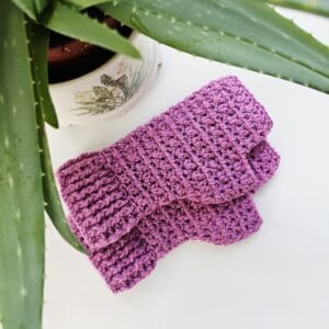Detail of the colour and even stitches of the Carnation Pink crochet mitts, laid out on a neutral background.