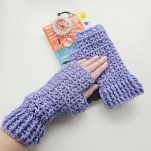 Close-up of a pair of handmade lilac crochet fingerless mitts, showing the intricate V-stitch pattern and ribbing around the wrist.