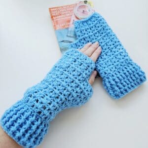 Detailed view of the ribbed cuff and thumbhole area of the sky blue acrylic fingerless glove, with an OS map and compass visible in the background.