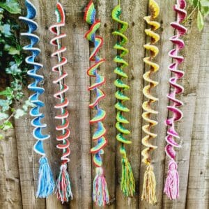 Wind Spinners made by Sarah Lou Crafts in five different designs of and colours show hanging from a wooden garden fence as ornaments and can also be used as window hangings.