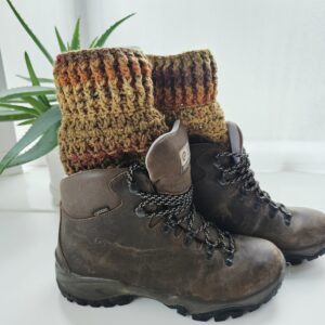 A pair of dark brown hiking boots shown from the side. A pair of crochet boot cuffs is visible showing the autumn colours of burnt orange and brown. The boot cuffs have a ribbed texture.