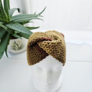 A detailed shot of the "turban-style" twist at the front of a autumn crochet headband. The chunky aran stitches create a braided effect where the fabric overlaps.