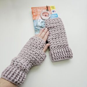 Detailed view of the ribbed cuff and thumbhole area of the pastel pink acrylic fingerless glove, with an OS map and compass visible in the background.