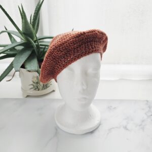 An front view of a circular crochet beret in spice orange. The design radiates from the centre in a starburst pattern, showing the crown’s symmetry and the rich, saturated colour of the British wool.