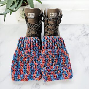 A pair of chunky, hand-crocheted boot toppers in bright neon shades, styled with sturdy brown walking boots against a neutral background.