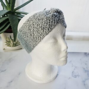 A three-quarter view of a marble grey ear warmer on a mannequin. The marble-effect yarn creates a mottled, stone-like pattern, and the headband’s width provides ample coverage for cold weather.